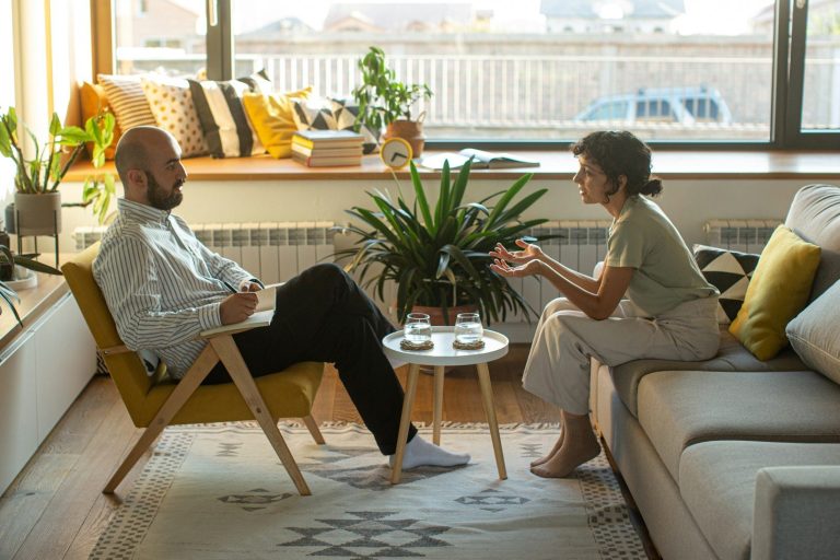 Sesión de Mediación Dos personas conversan en una sala acogedora, rodeadas de plantas y luz natural.